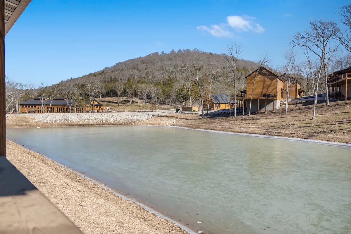 A serene lake scene features calm water bordered by rolling hills and rustic wooden cabins. The early morning fog rises from the water, creating a peaceful atmosphere ideal for kayaking, paddle boarding, or simply enjoying the lake’s beauty after a hike on nearby trails.