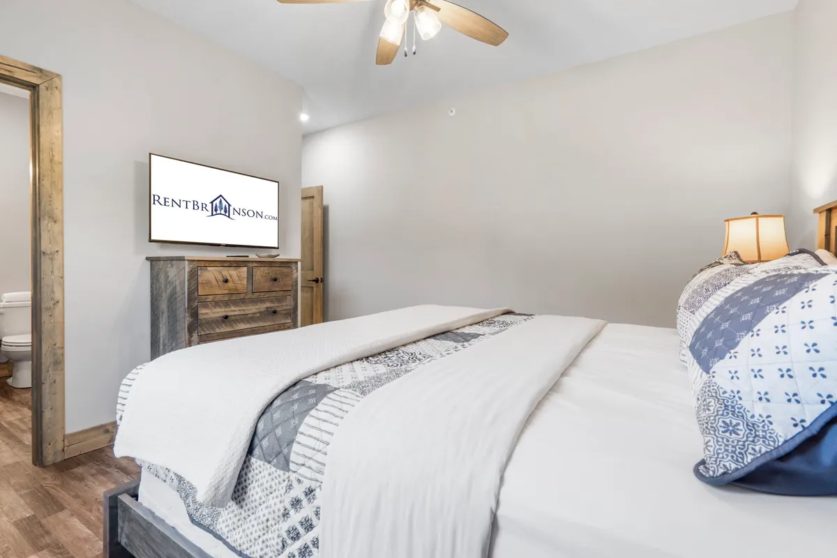 A comfortable king bedroom with patterned throw bedding, a wooden dresser, and a flat-screen TV. The arrangement emphasizes both relaxation and entertainment within a serene setting.