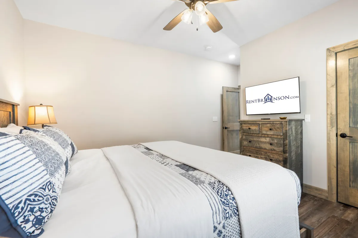 This image showcases a king bedroom featuring a bed with decorative bedding, a wooden dresser, a bedside lamp, and a wall-mounted television. The room exudes a relaxing and comfortable atmosphere, inviting guests to unwind and enjoy their privacy.