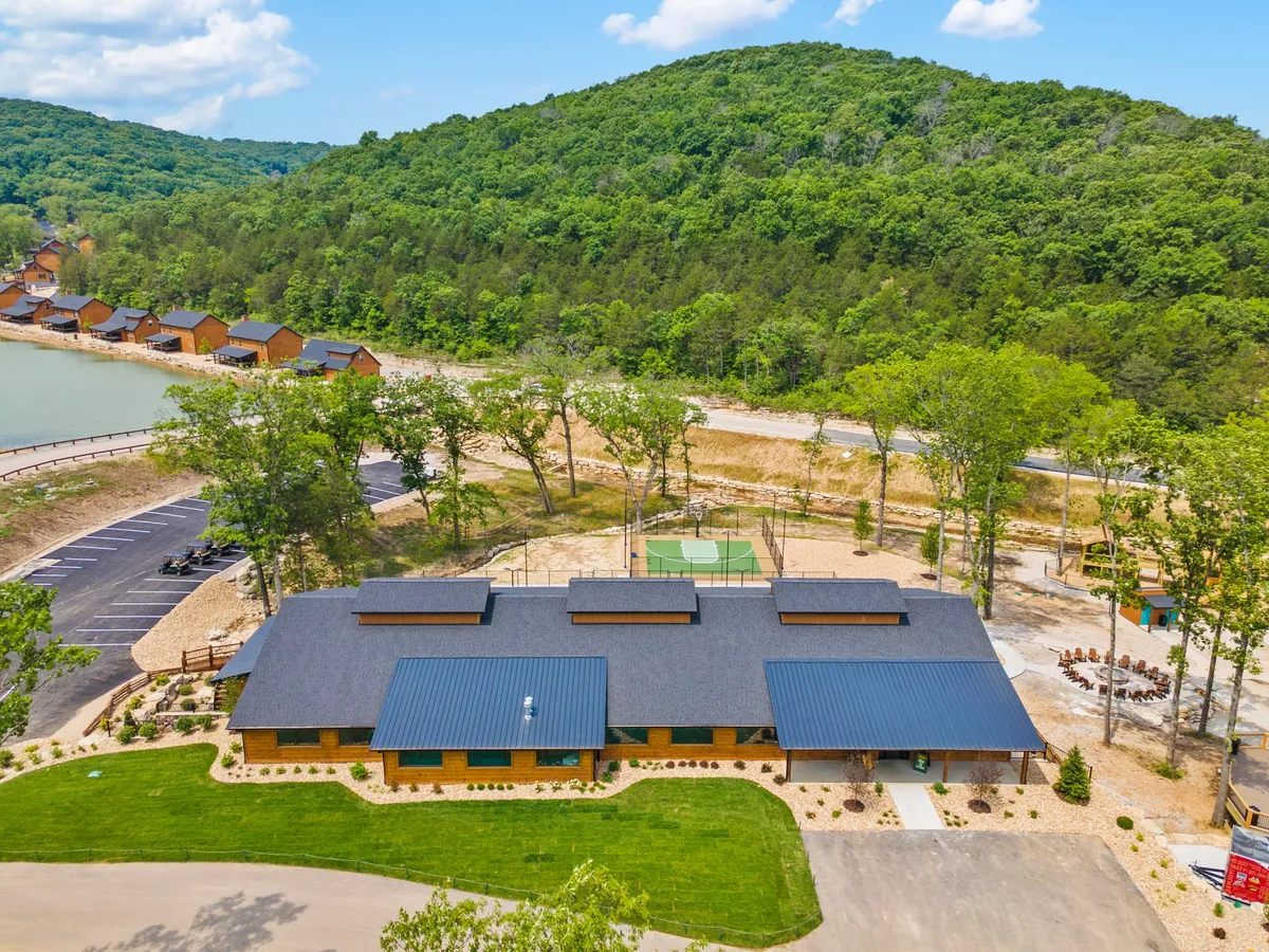 A sweeping exterior view shows the main building of Tall Timbers Camp with its picturesque lakeside location, basketball court, picnic area, and mountain vistas. The grounds are inviting and set up for both active play and quiet relaxation.