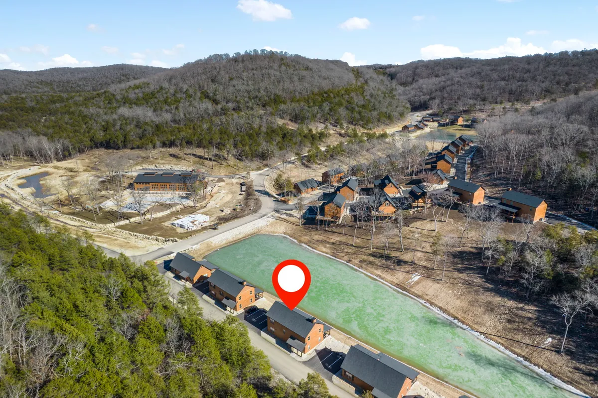 A peaceful scene showing a cluster of cabins near a body of water, surrounded by rolling hills and woodlands. The natural setting is undisturbed, with the water reflecting the calm sky, inviting moments of stargazing and wildlife watching.