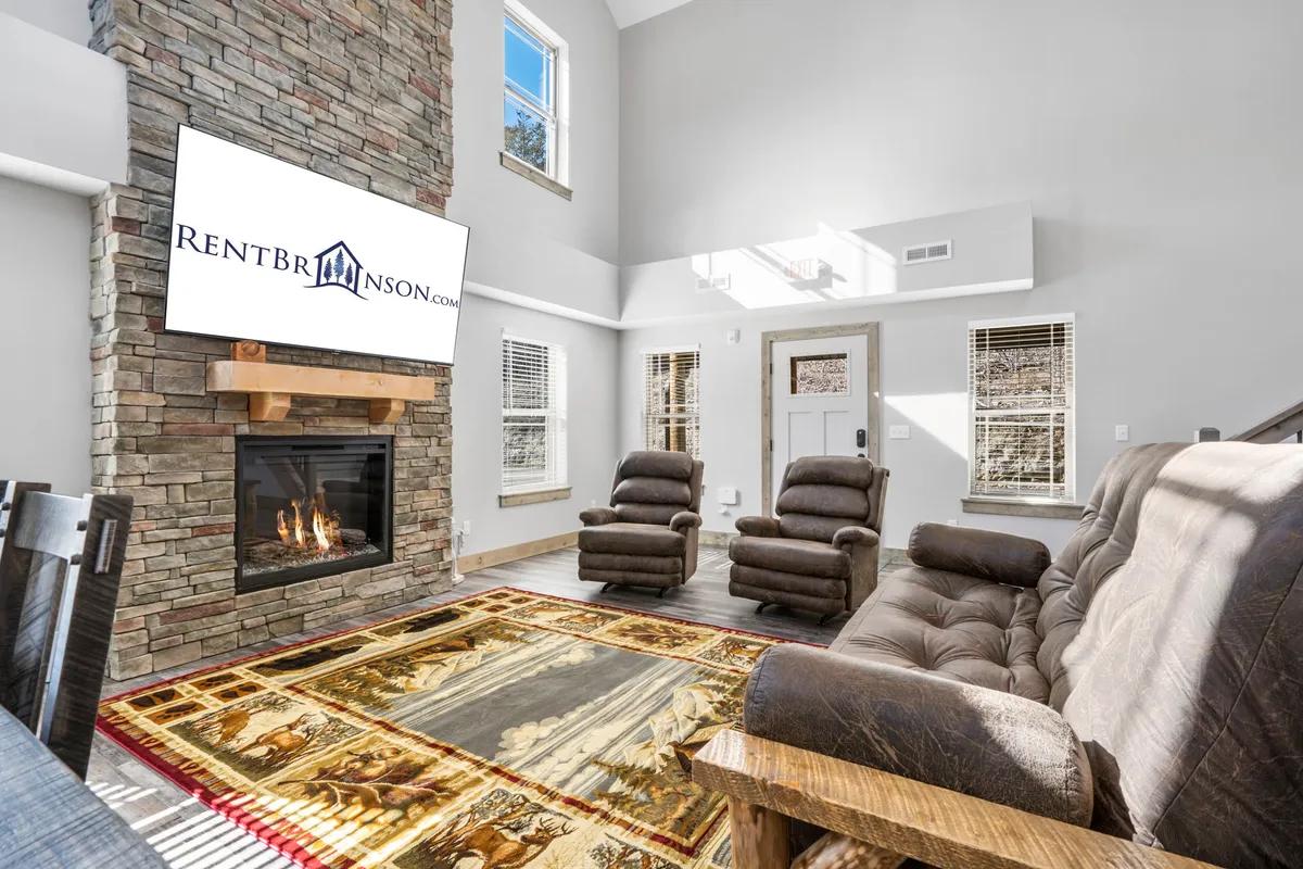 The image captures a warm, inviting living room featuring a grand stone fireplace as the centerpiece, surrounded by plush, comfortable seating and a large television. The space is accented with a stylish area rug, creating an atmosphere perfect for gatherings, movie nights, or relaxing by the fire.