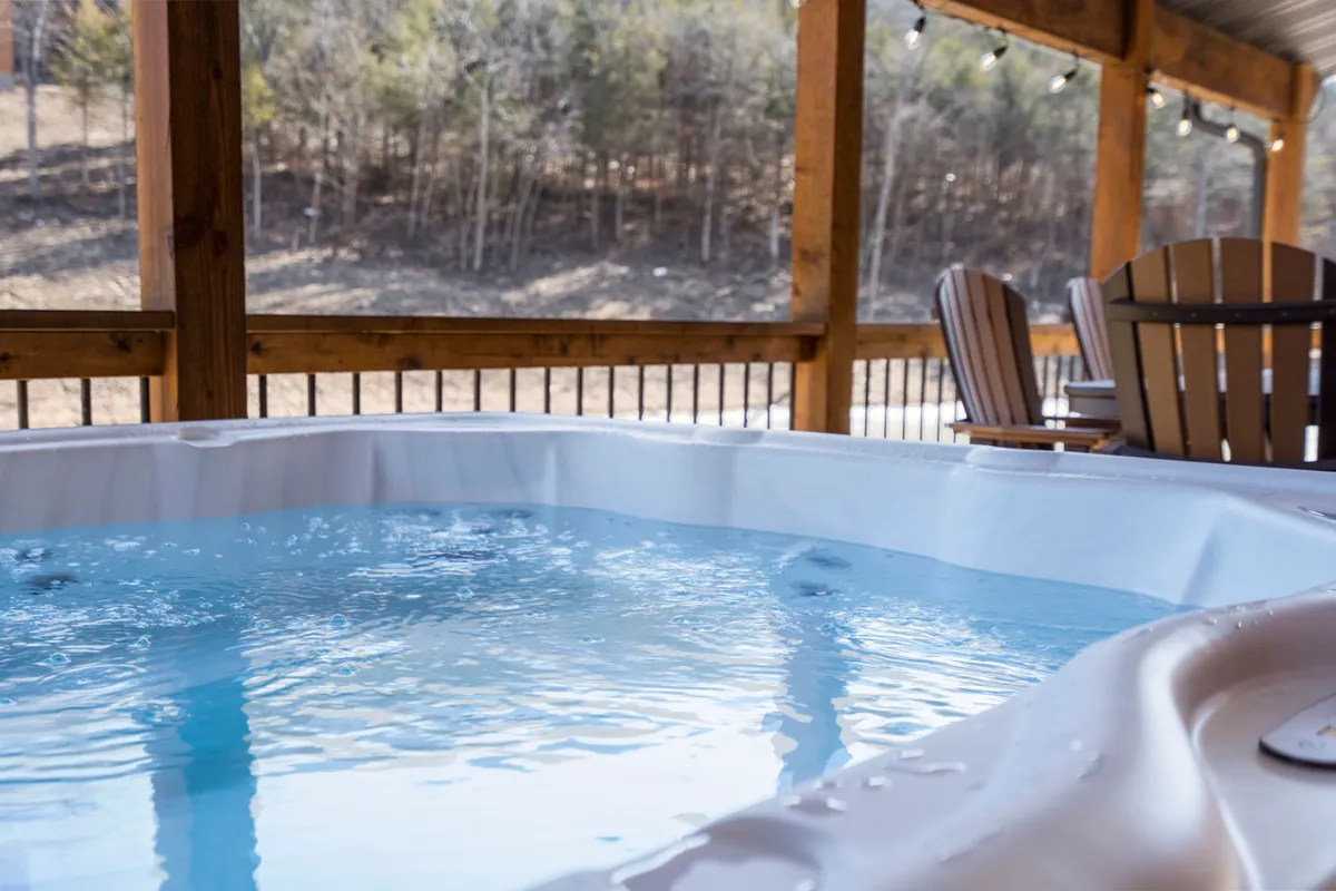 A tranquil wooden deck nestled in nature, featuring a bubbling hot tub positioned to overlook the surrounding pines. The deck is spacious and offers comfortable seating, ideal for soaking in the views or relaxing after a day of adventure.