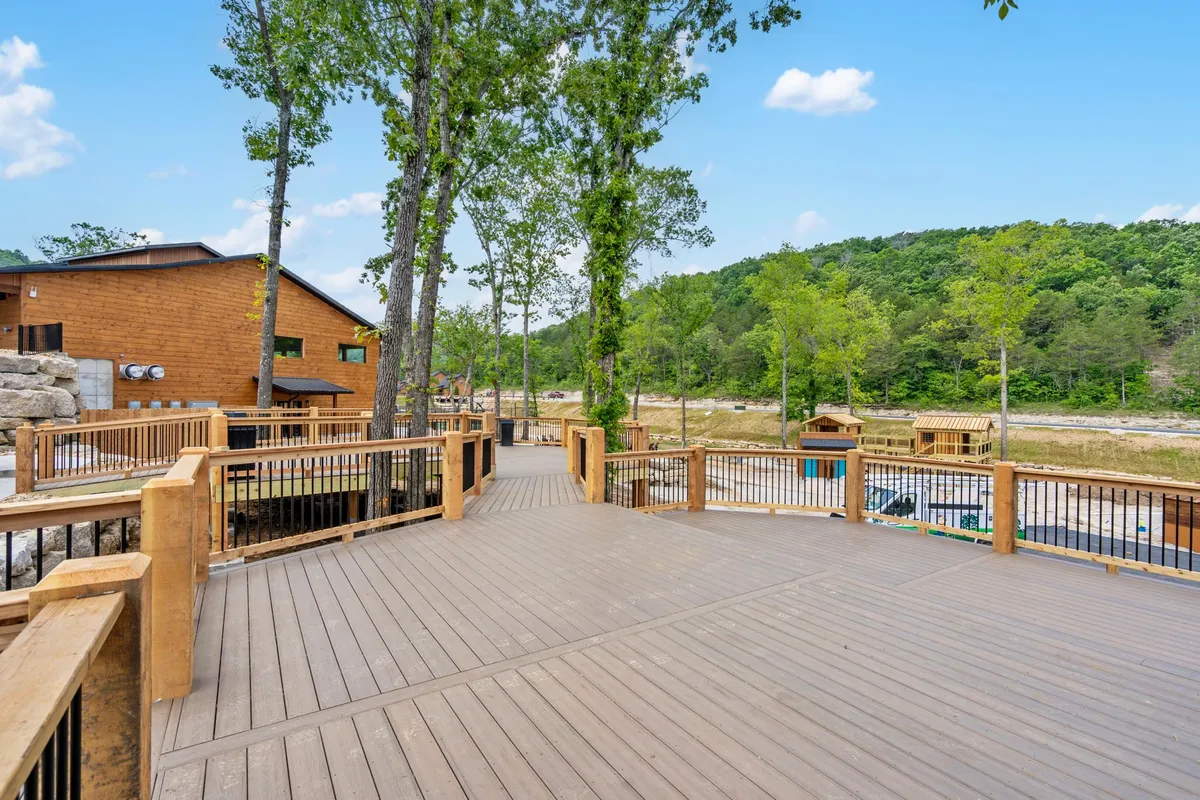 A wide wooden deck stretches out from a private lodge, surrounded by tall trees and distant rolling hills. The setting sun bathes the area in a warm glow, inviting moments of relaxation, barbecues, and wildlife observation. The scene captures the peaceful, private side of the lodge experience, emphasizing a direct connection to nature.