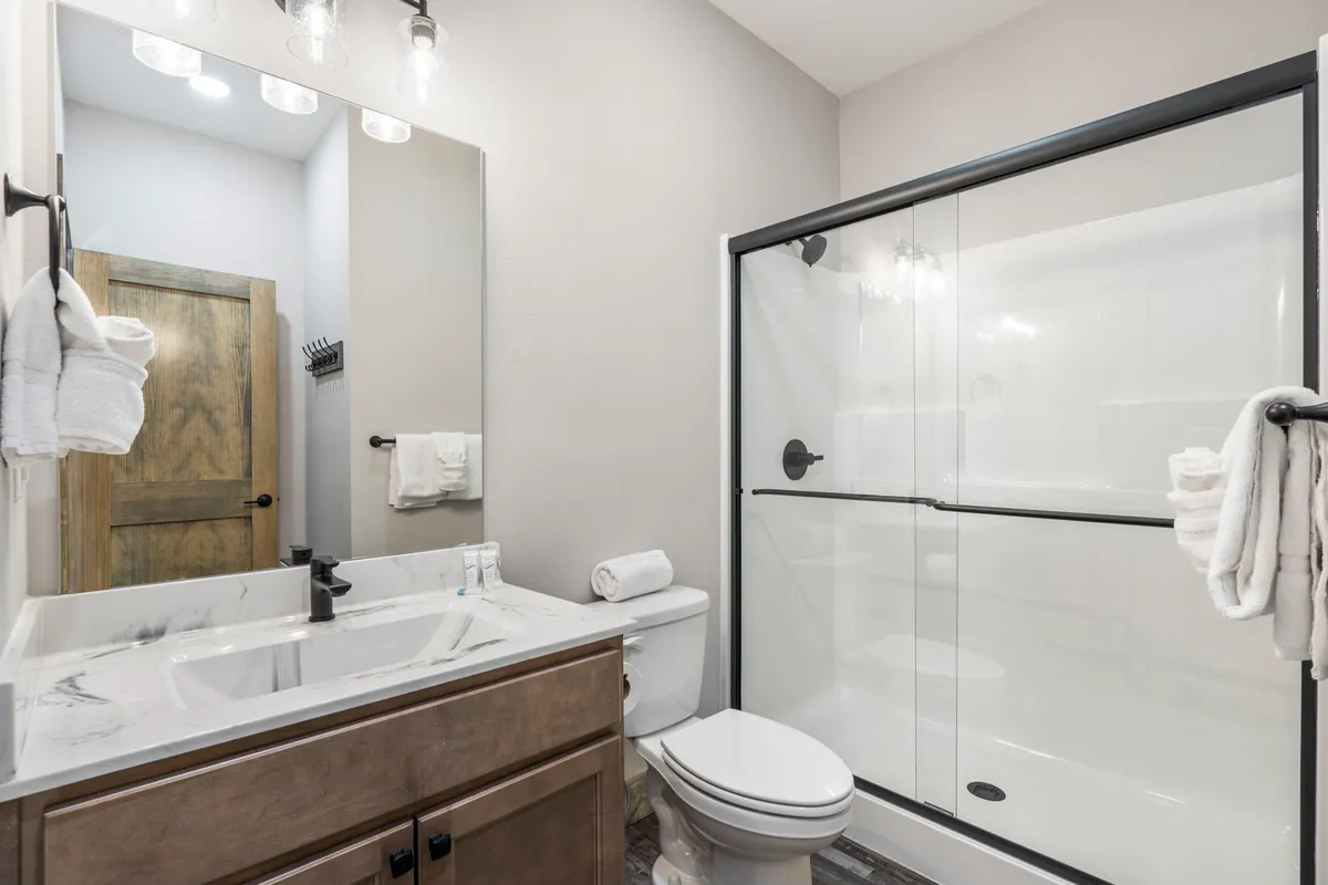 A contemporary en-suite bathroom with a marble countertop, glass shower enclosure, large mirror, and wooden cabinet. The space is serene and inviting, perfect for self-care and rejuvenation.