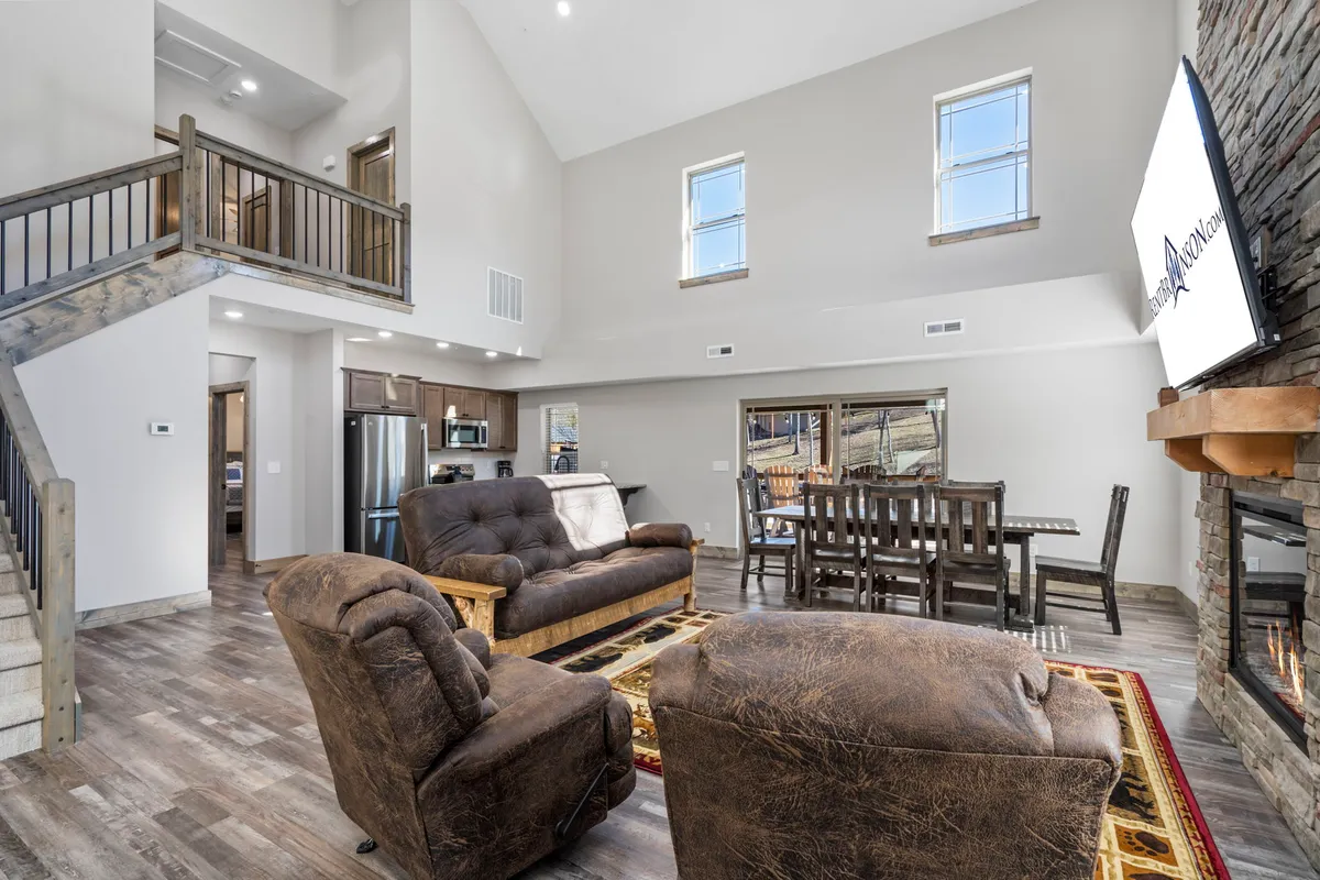 A warm, welcoming interior featuring a cozy sofa, dining table, stone fireplace, and expansive windows that frame tranquil outdoor views. The space is set up for family meals, relaxation, and togetherness, with a seamless blend of comfort and style.