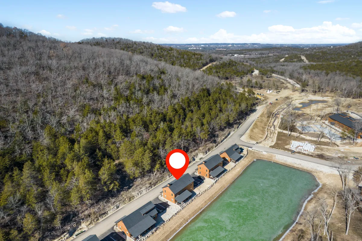 This image captures cabins along the tranquil edge of a pond, surrounded by lush greenery. The water’s surface glimmers in the natural light, and the setting evokes an inviting sense of calm and connection to nature. This is an ideal spot for fishing, hiking, and relaxing by the water, with trails disappearing into the woodland beyond.