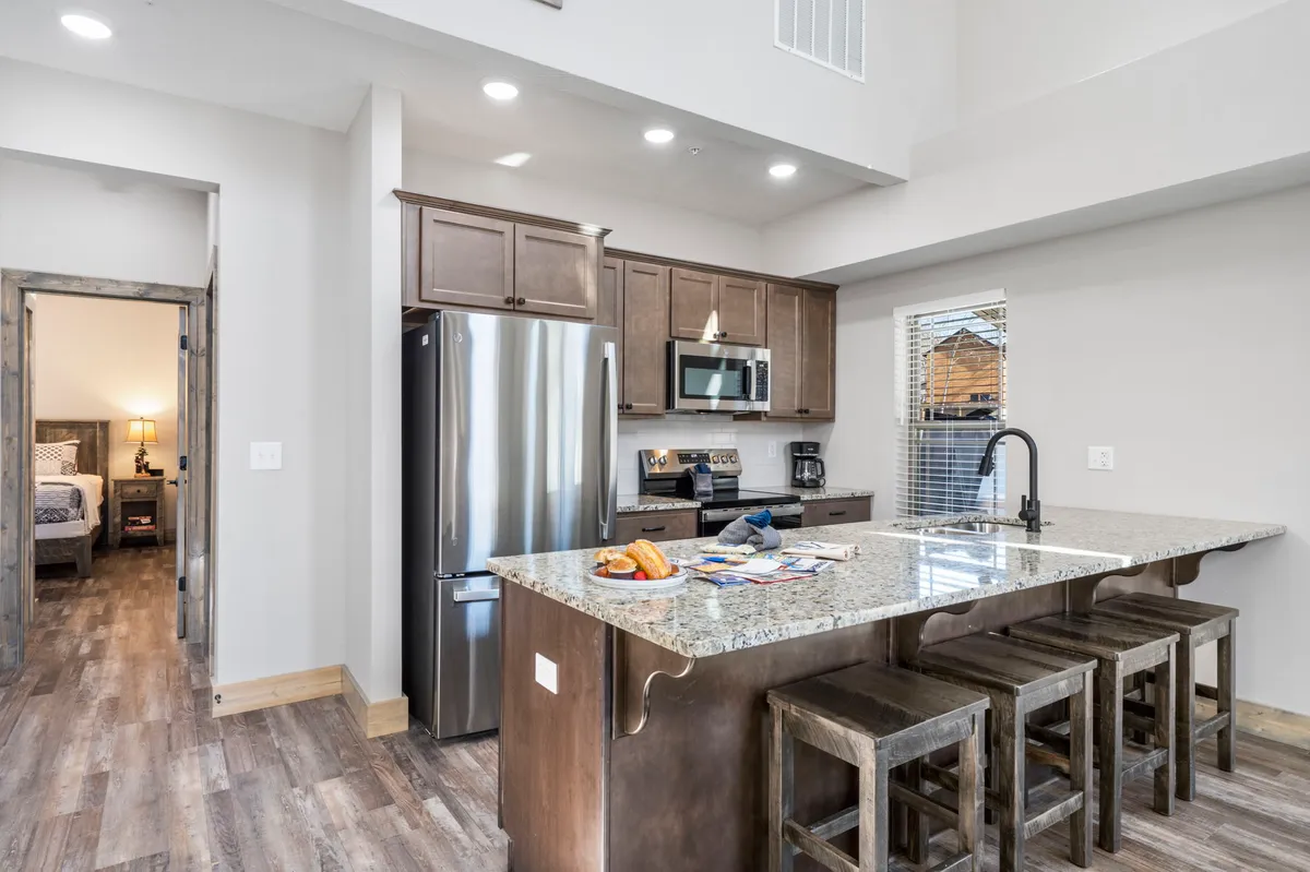 A modern kitchen with a large granite island countertop, stainless steel appliances, and wooden seating stools. The design invites social cooking and casual conversation, with ample workspace and high-end finishes for any culinary adventure.